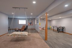 Remodeled basement with large open space. An area off to the side of the room has a shuffle board and cornhole board for entertaining. Left side of the room has seating for guests