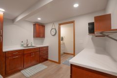 Newly remodeled basement designed as a laundry room. White countertops and a sink on the back wall. Side of the room looks to go into a bathroom