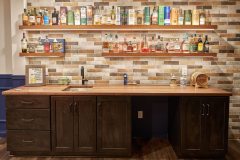 Wall of alcohol for a basement home bar setup with newly designed wall tile and a counter underneath with a sink