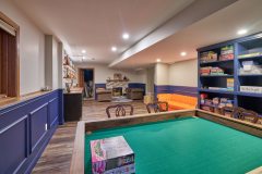 Newly remodeled basement showing a small green table, side walls with built in storage and open entertaining area