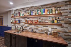 Wall of alcohol for a basement home bar setup with newly designed wall tile and a counter underneath with a sink