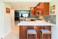 Remodeled kitchen example with new white countertops and dark wood stained cabinets. Two barstools are facing the camera