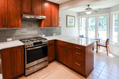 Remodeled kitchen example with new white countertops and dark wood stained cabinets. Stainless steel new oven and a small table and chairs in the back with long windows for backyard viewing