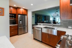 Remodeled kitchen example with new white countertops, dark wood stained cabinets, and new stainless steel appliances. A layered bar top separates the room from the back living area.