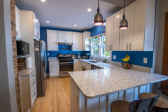 modern kitchen remodeled with grey and white granite counters, white cabinets, new steel appliances and lighting fixtures. The walls are painted blue