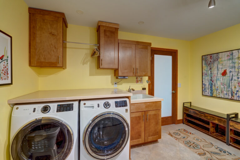 Laundry room remodel with new appliances and large countertop above the washer and dryer for easy folding. Light brown wood cabinets with a large sink.